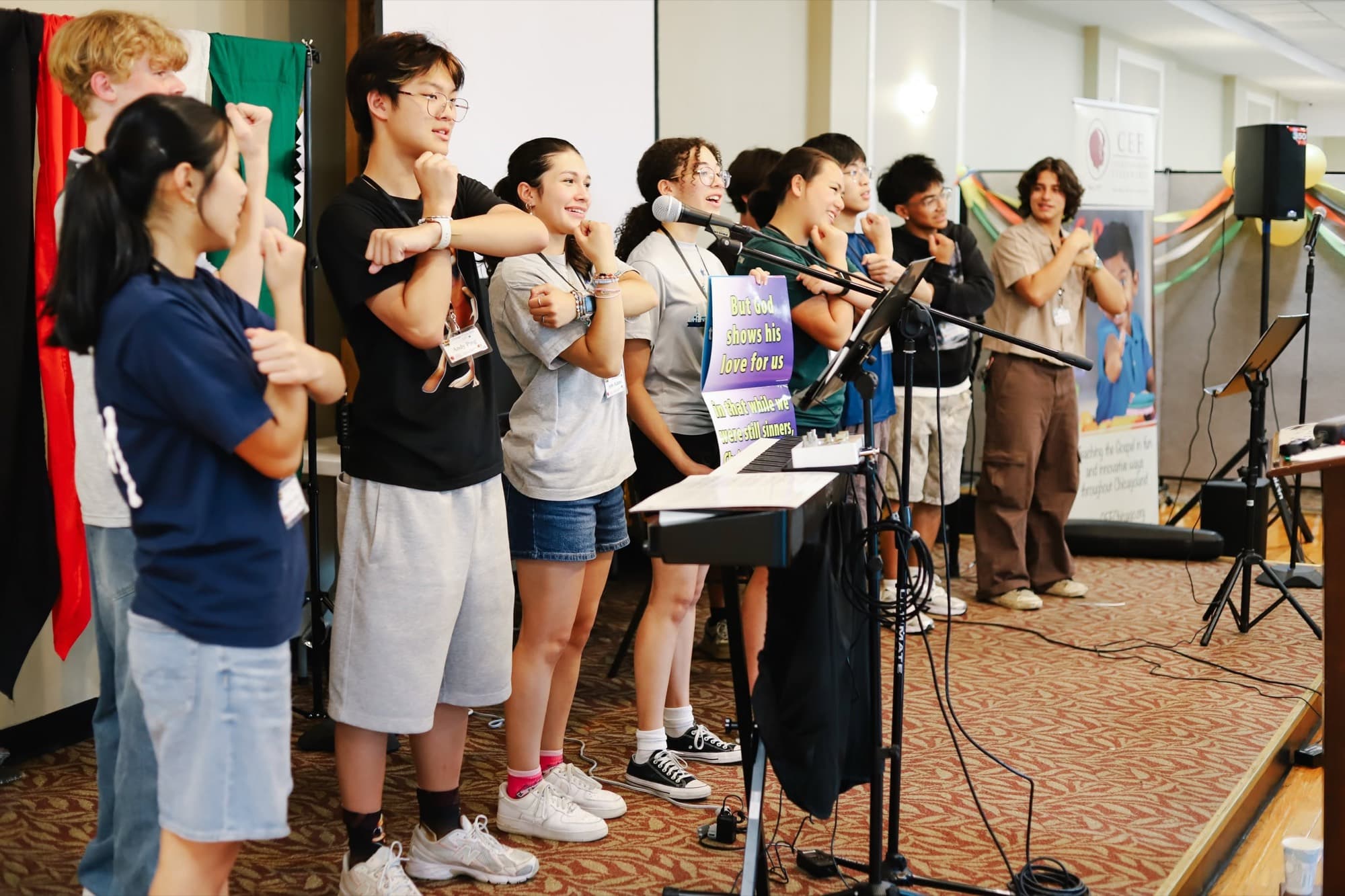 Teenagers stand and sing together beside a keyboard