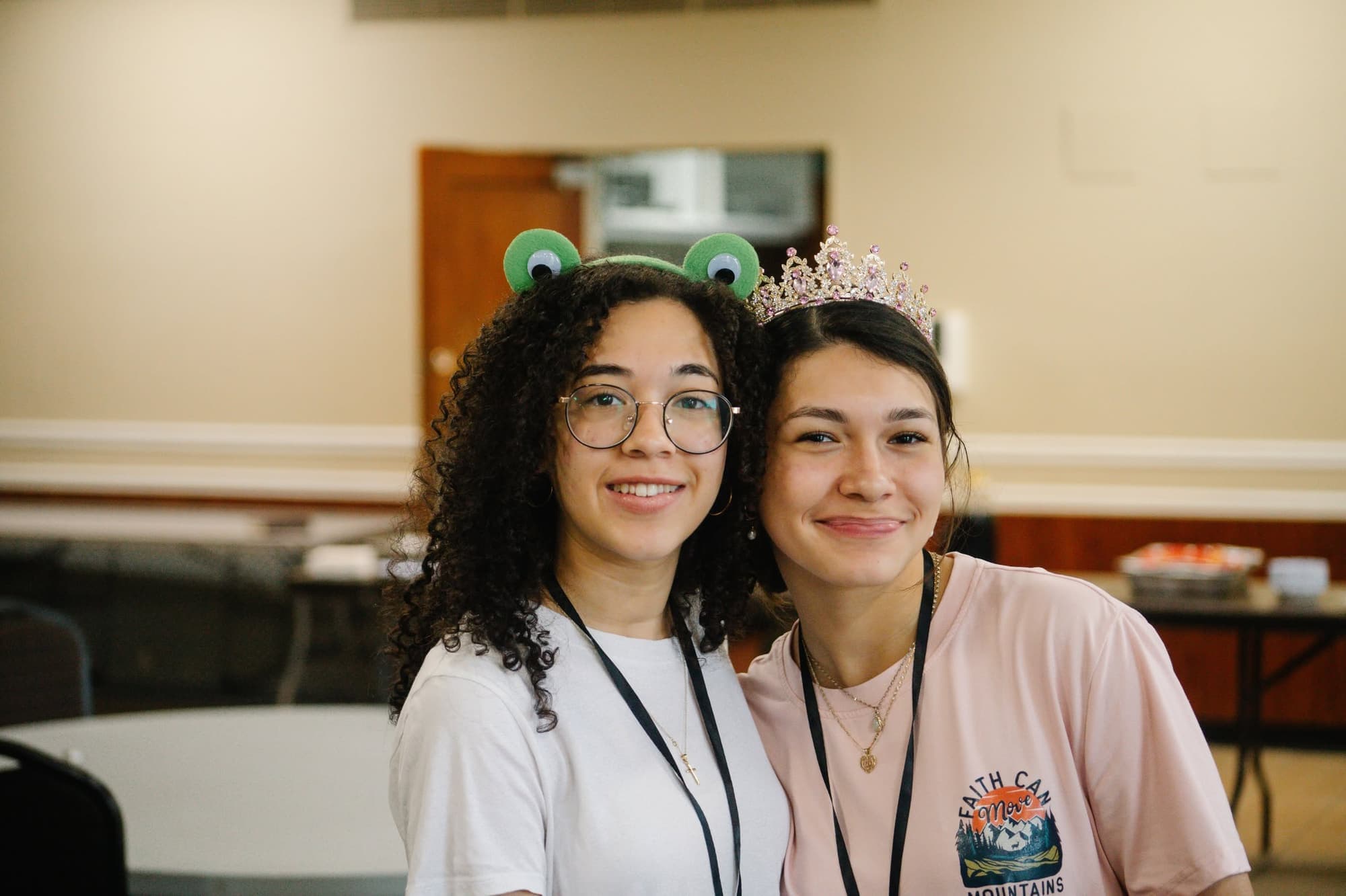 Two teenagers wearing lanyards smile with their heads together
